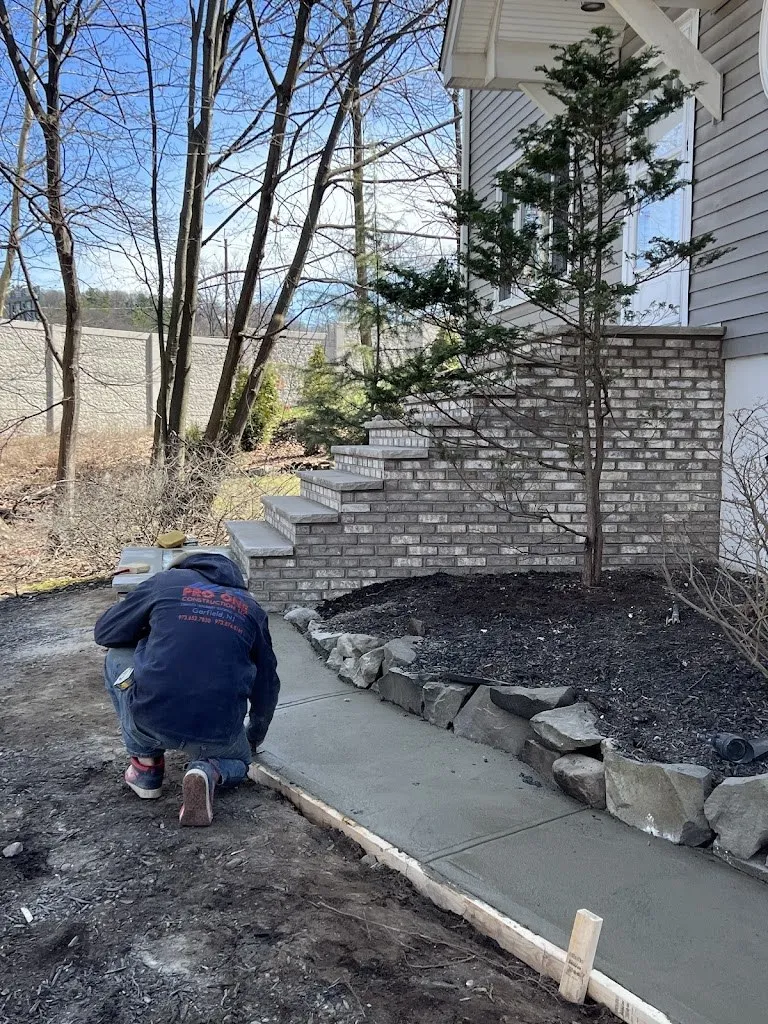 Pro One mason finishing a new concrete walkway beside brick steps