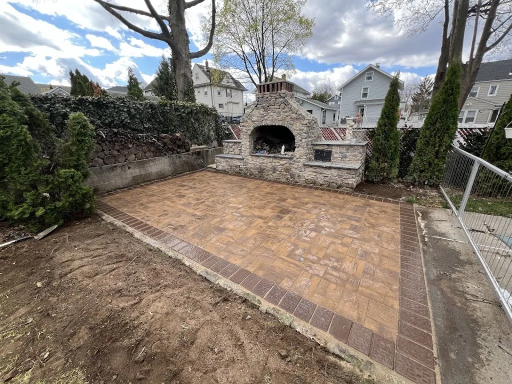 Stone outdoor fireplace and chimney at the end of a new paver patio in a fenced backyard
